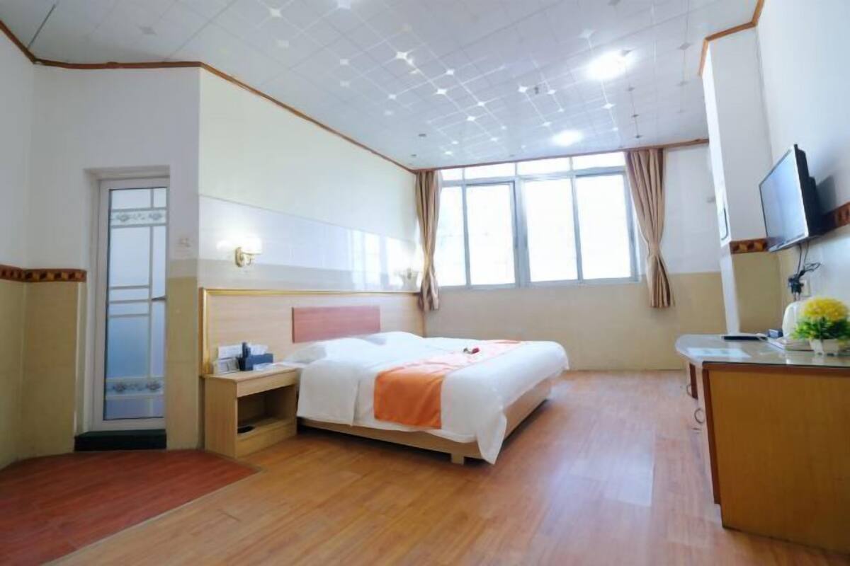 Habitación de hotel con cama, mesita de noche, televisión y ventana con cortinas.
