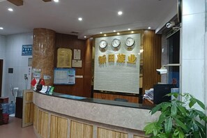A reception desk with a clock, a bulletin board, and a plant. - Xintian Lvye Hotel (Foshan)
