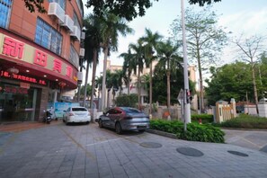 A street with parked cars and a building with a red sign. - Xintian Lvye Hotel (Foshan)
