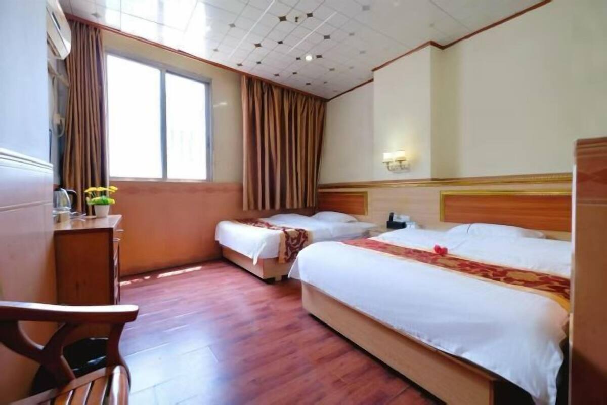 Habitación de hotel con dos camas, un escritorio, una silla, una ventana con cortinas y un techo con diseño de cuadrícula.