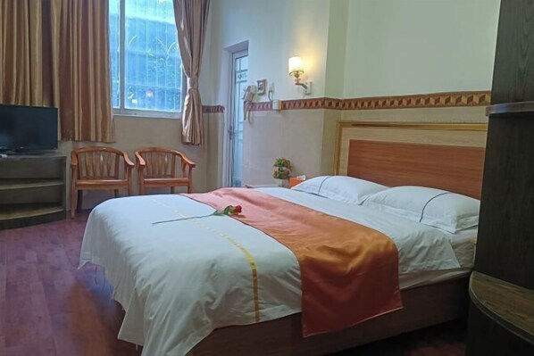A hotel room with a bed, a television, two chairs, a window with curtains, and a wall-mounted light fixture. - Xintian Lvye Hotel (Foshan)