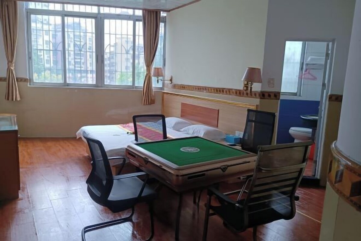 A hotel room with a bed, a desk with a computer, a chair, and a table with a green mat.