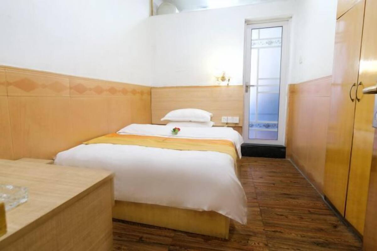Una habitación de hotel con piso de madera, una cama con ropa de cama blanca, una mesita de noche y un armario.