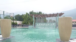 A swimming pool with two large stone sculptures, a pergola, and a view of mountains in the background. - The Wave International Resort, Jamshedpur (Golmuri)