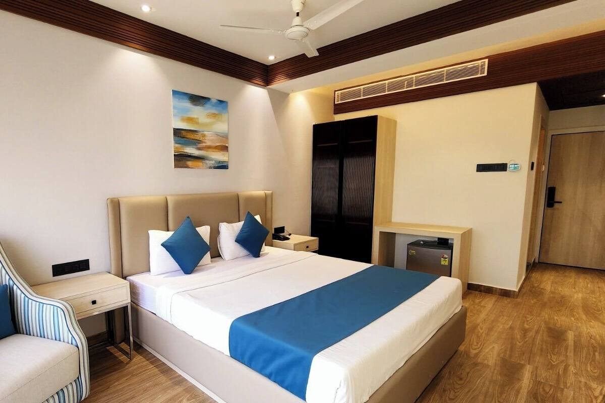 A hotel room with a bed, a chair, a desk, a wardrobe, and a ceiling fan.