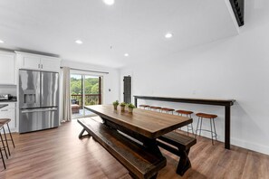 A modern kitchen with a wooden dining table, bar stools, and a stainless steel refrigerator.