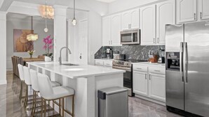 Cozinha moderna com armários brancos, eletrodomésticos de aço inoxidável e painel de backsplash de mármore.