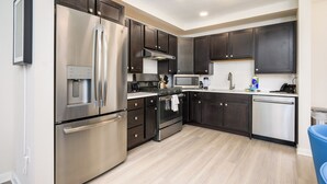 A modern kitchen with stainless steel appliances, dark cabinetry, and a light wood floor. - Brand New Modern Vista Cay Reserve Condo - 5008 (Orlando)