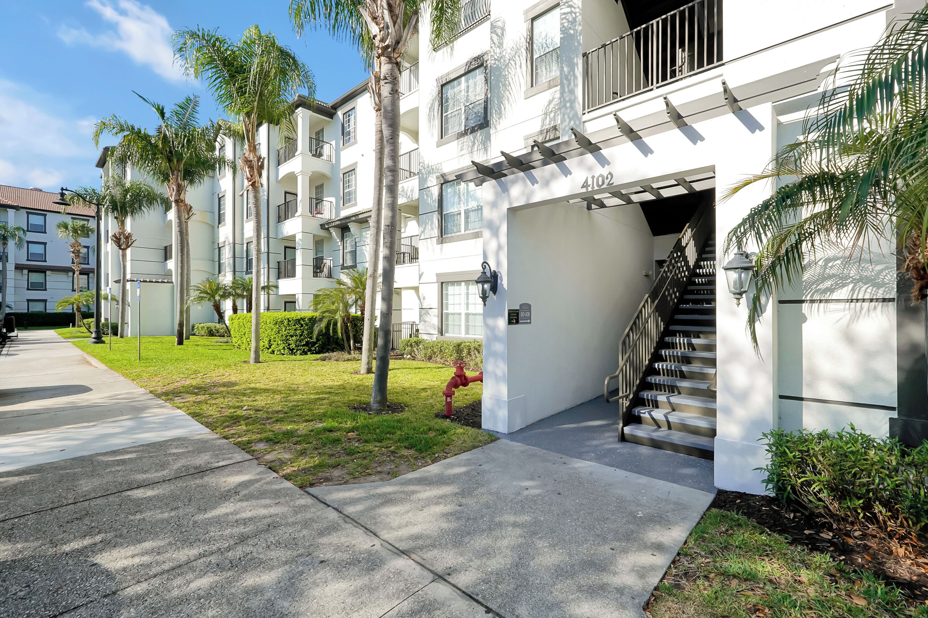A multi-story residential building with a covered entrance, a red fire hydrant, and a clear sky.