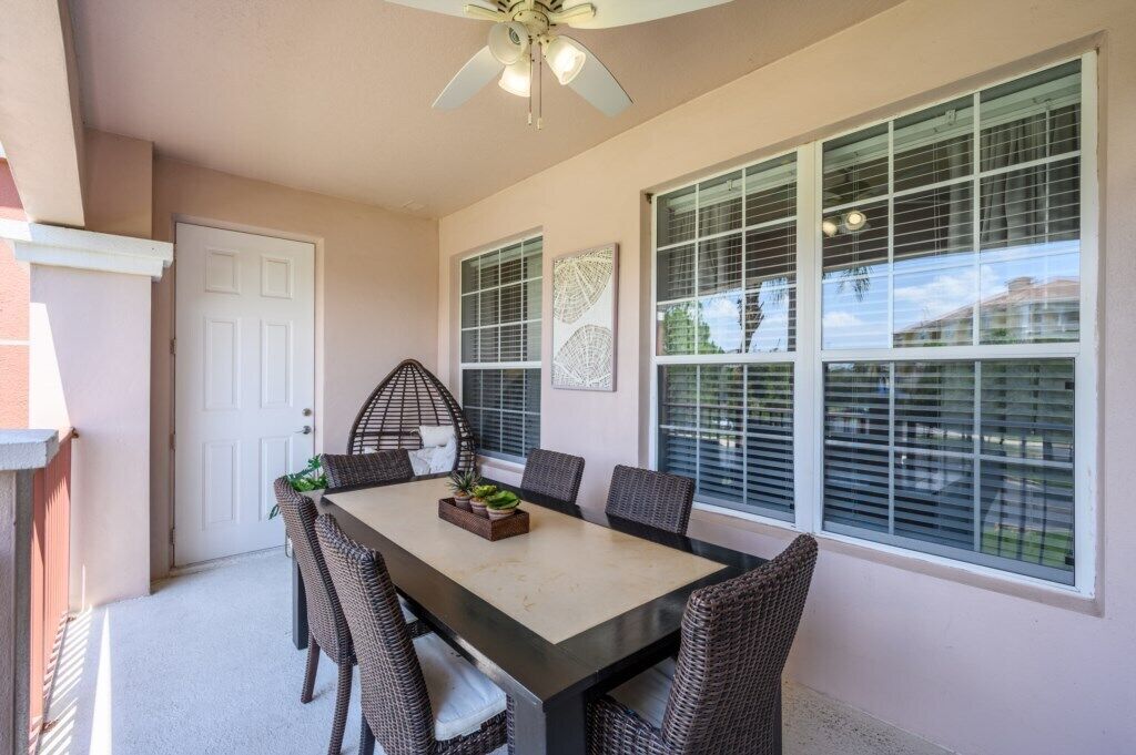 A dining area with a table and chairs, a ceiling fan, and large windows with blinds.