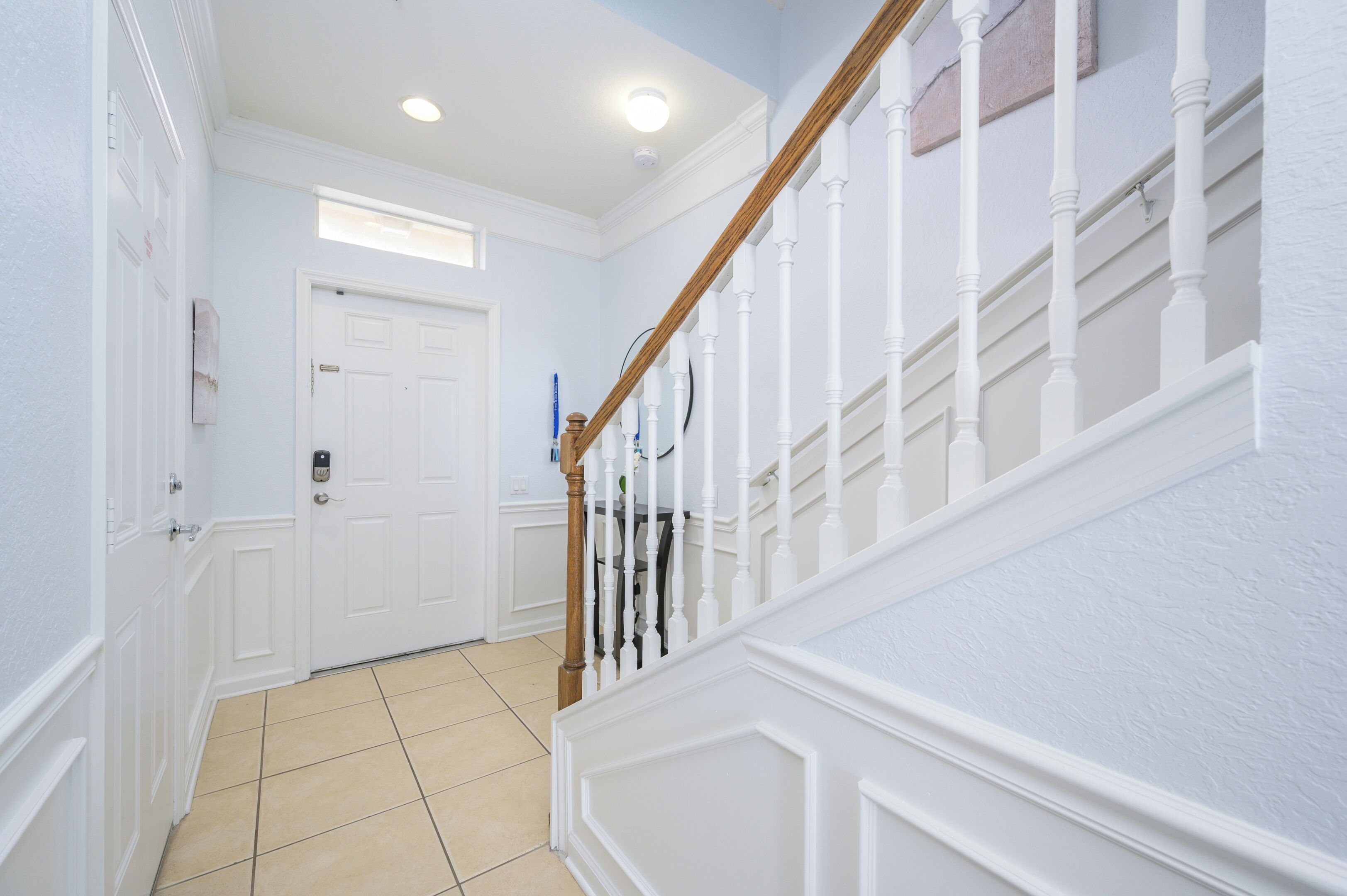 A hallway with white walls, a wooden staircase, and a door with a keypad lock.