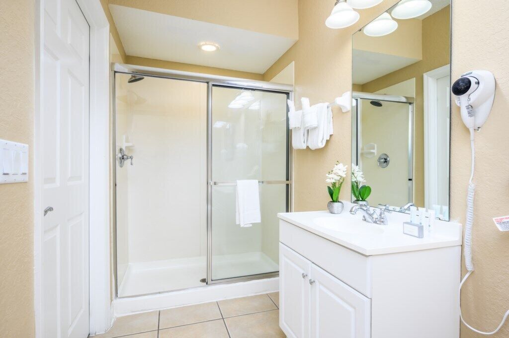 A modern bathroom with a glass-enclosed shower, a white vanity, a hairdryer, and a mirror.