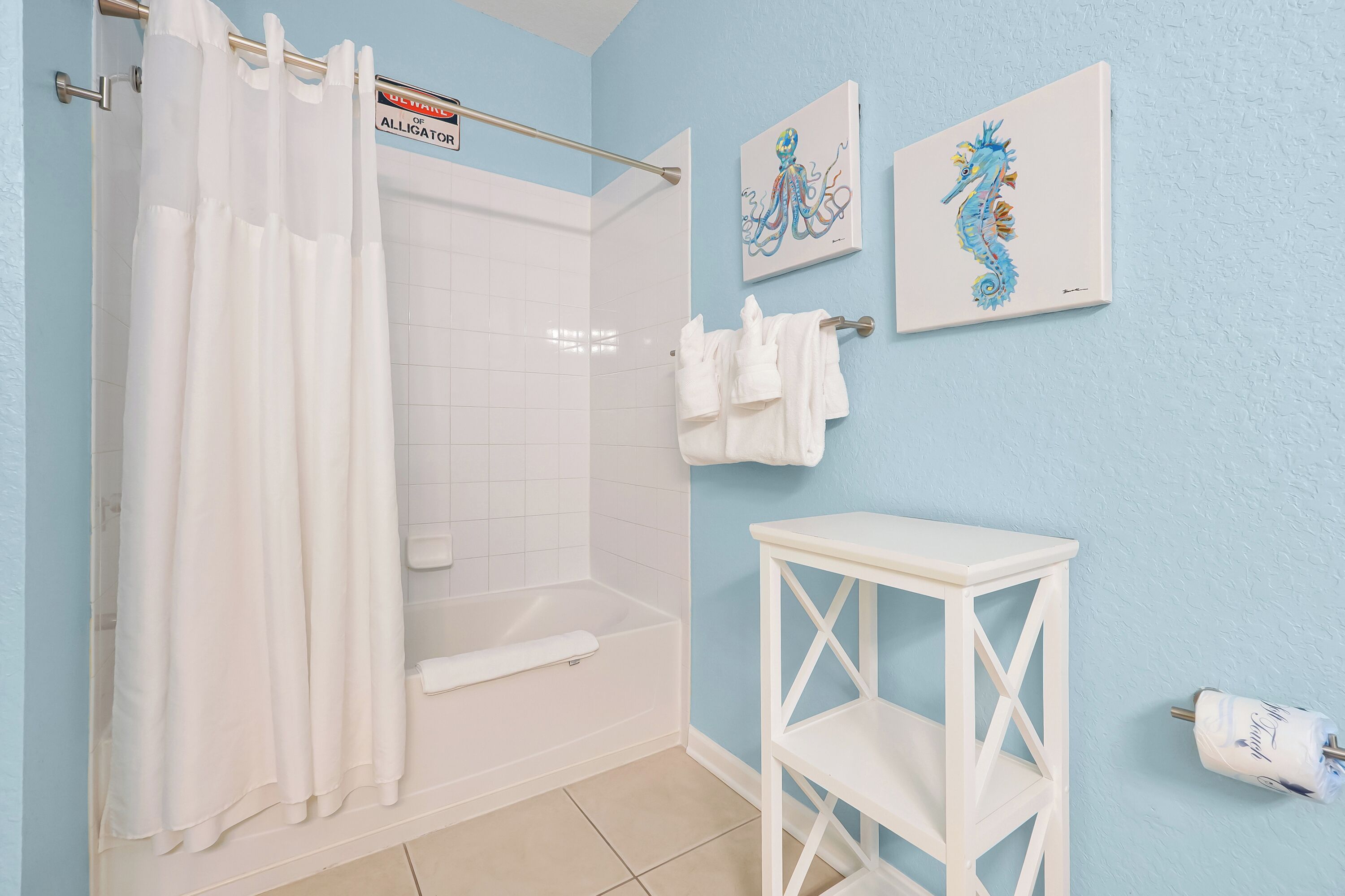 Ein Badezimmer mit Duschvorhang, Badewanne, einem weißen Regal und zwei gerahmten Bildern an der Wand.