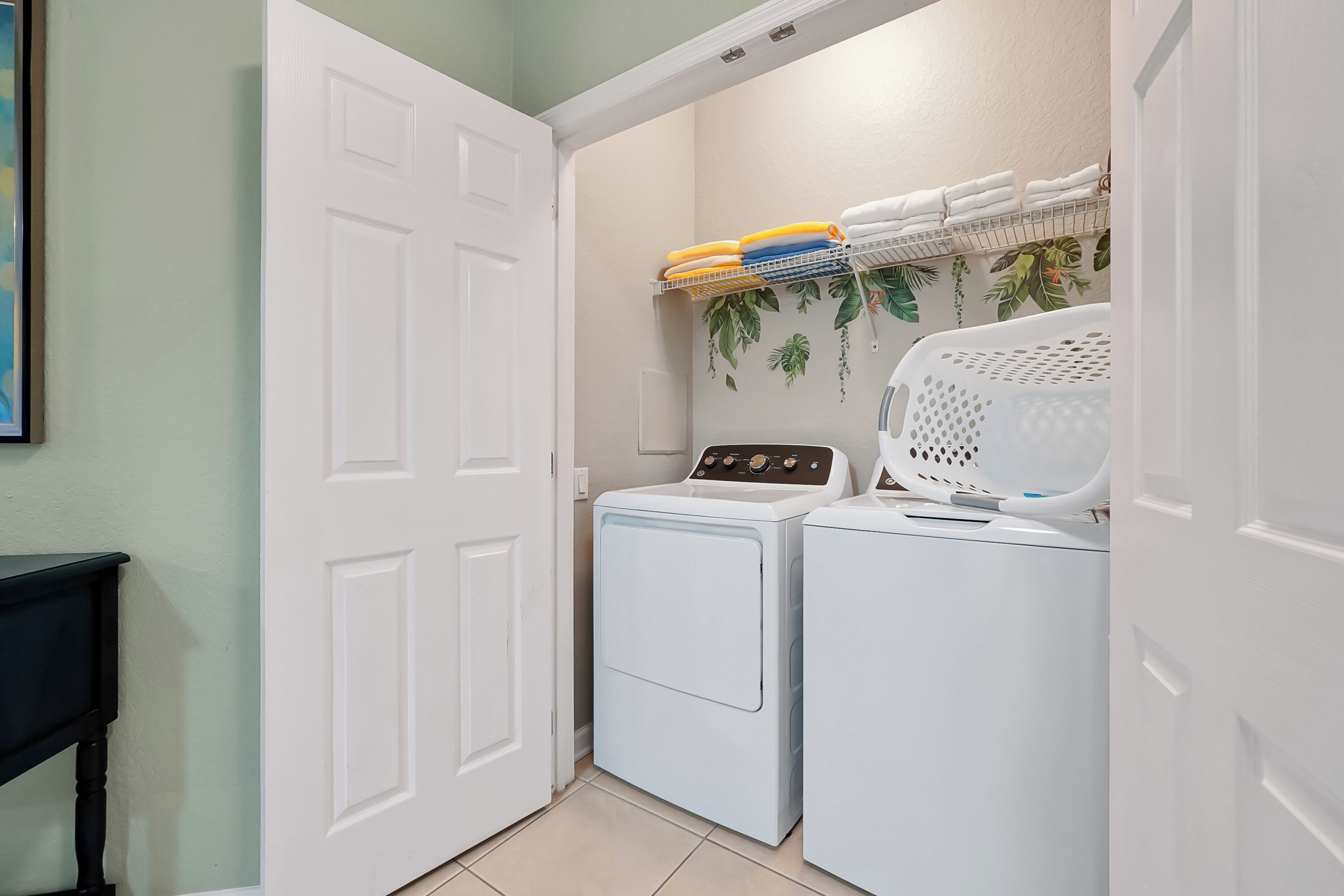 A laundry room with two washing machines, a drying rack with folded towels, and a wall-mounted shelf with towels.