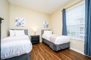 A hotel room with two beds, a nightstand with a lamp, and artwork on the walls.