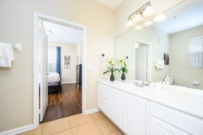 A modern bathroom with a large mirror, white vanity, and a shower area visible through an open door.