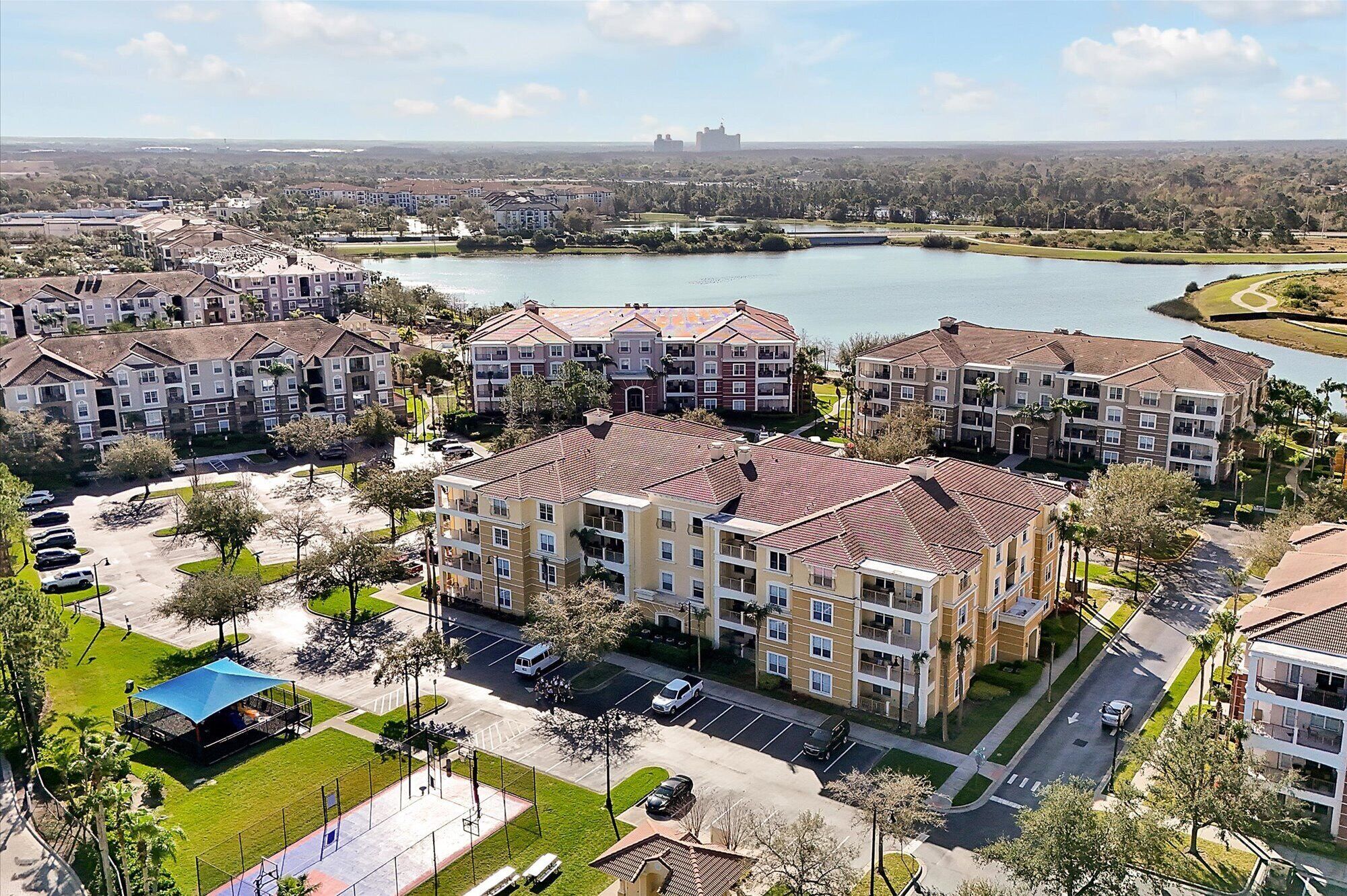 Zona residencial con edificios de apartamentos, un estacionamiento y un lago al fondo.