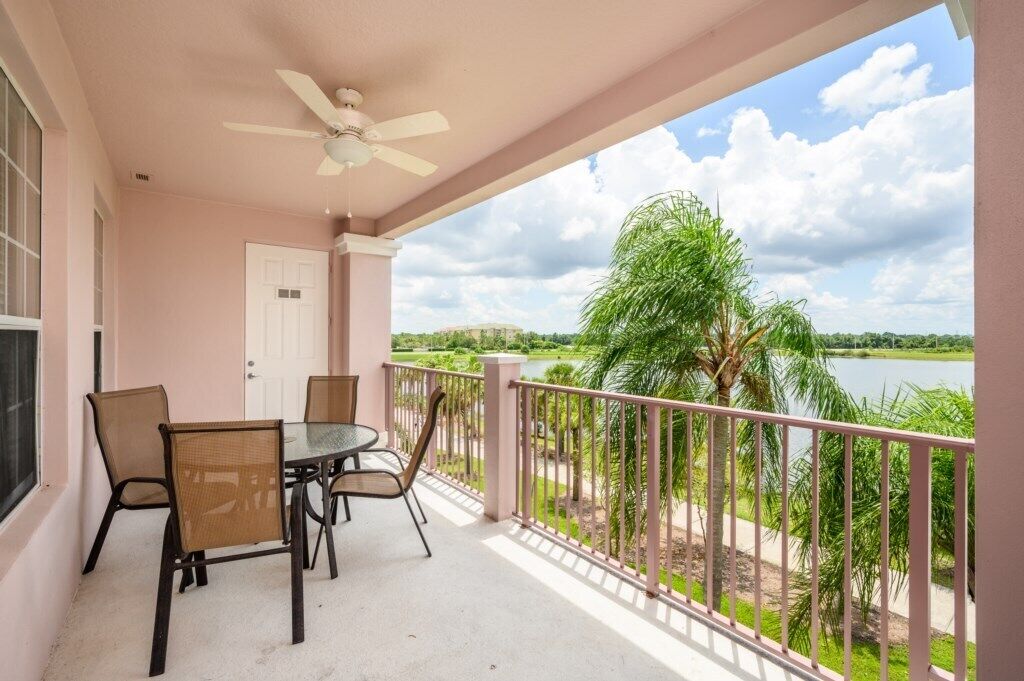 Un balcon avec une table et des chaises, un ventilateur de plafond et une vue sur un lac et la verdure.