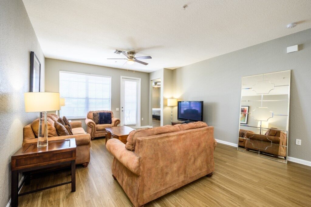 A living room with a sofa, armchair, coffee table, TV, and a ceiling fan.
