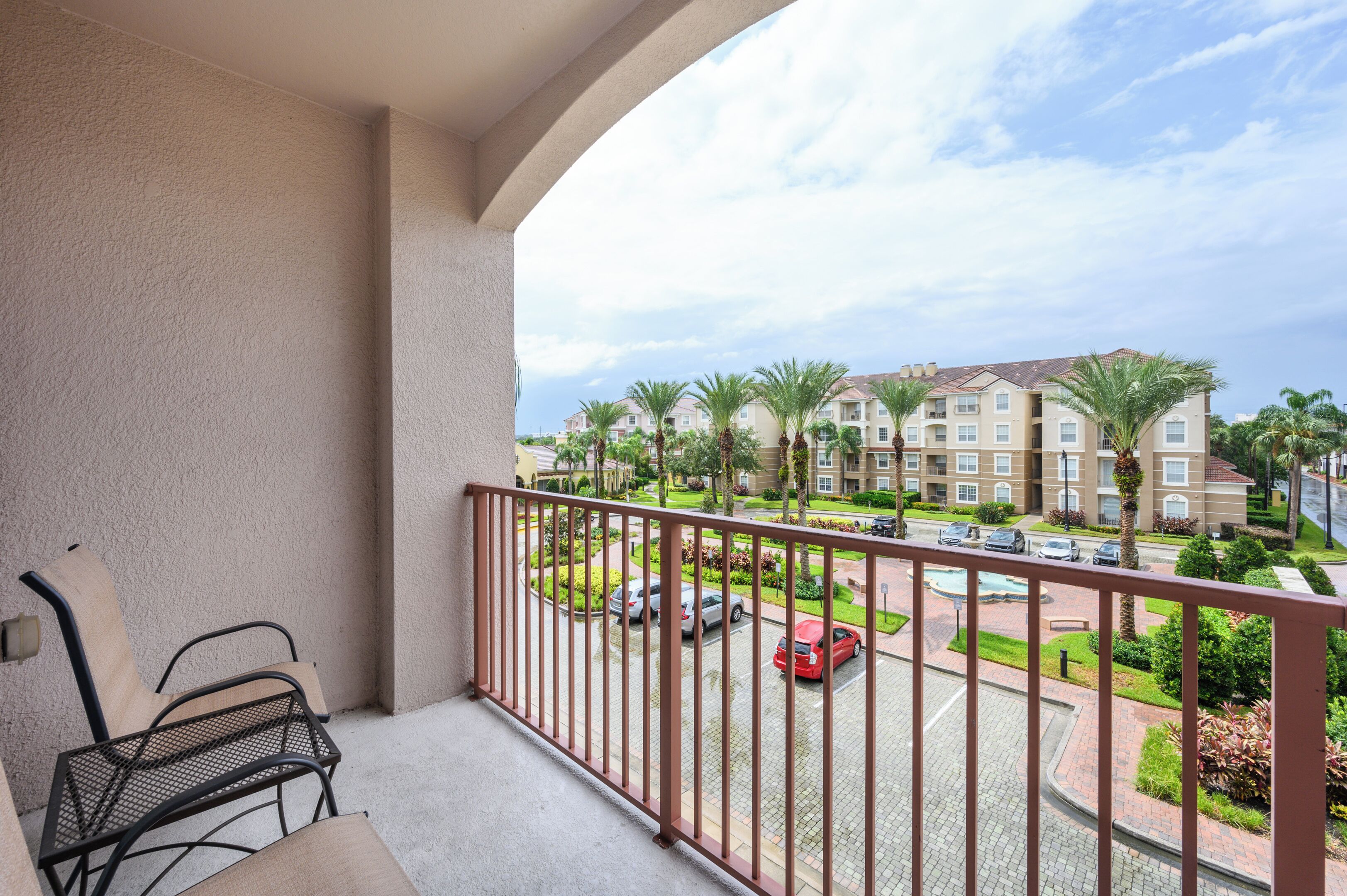 A balcony with a view of a residential area, including a parking lot and a building with multiple floors.