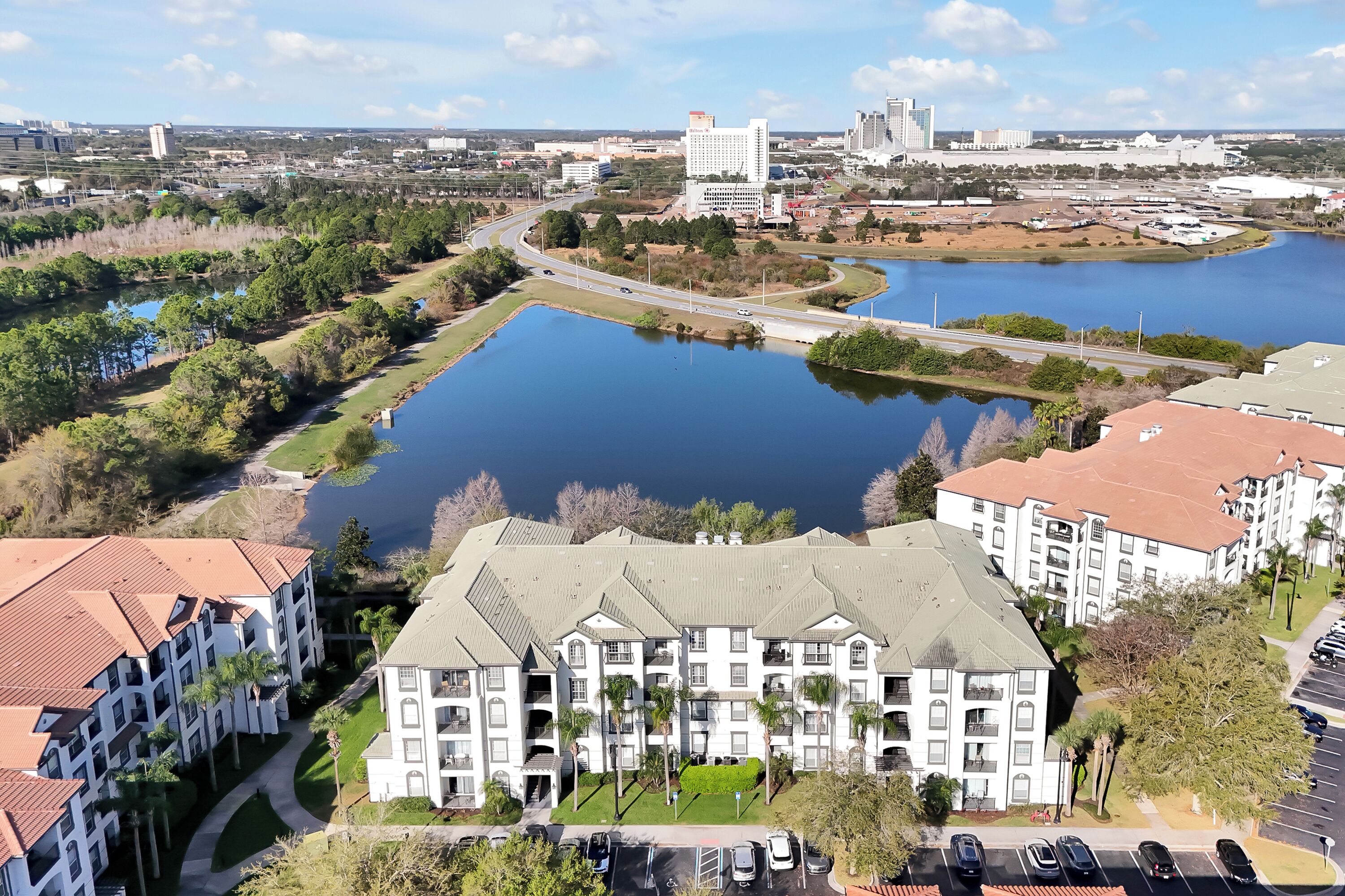 A multi-story hotel with a central courtyard, parking, and a view of a lake and surrounding cityscape.
