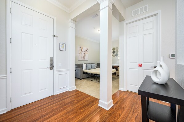 Un couloir avec un plancher en bois, des portes blanches et un coin repas comprenant un canapé gris et un vase blanc posé sur une table.