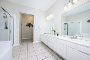 A modern bathroom with a large mirror, two sinks, a shower, and a tiled floor.