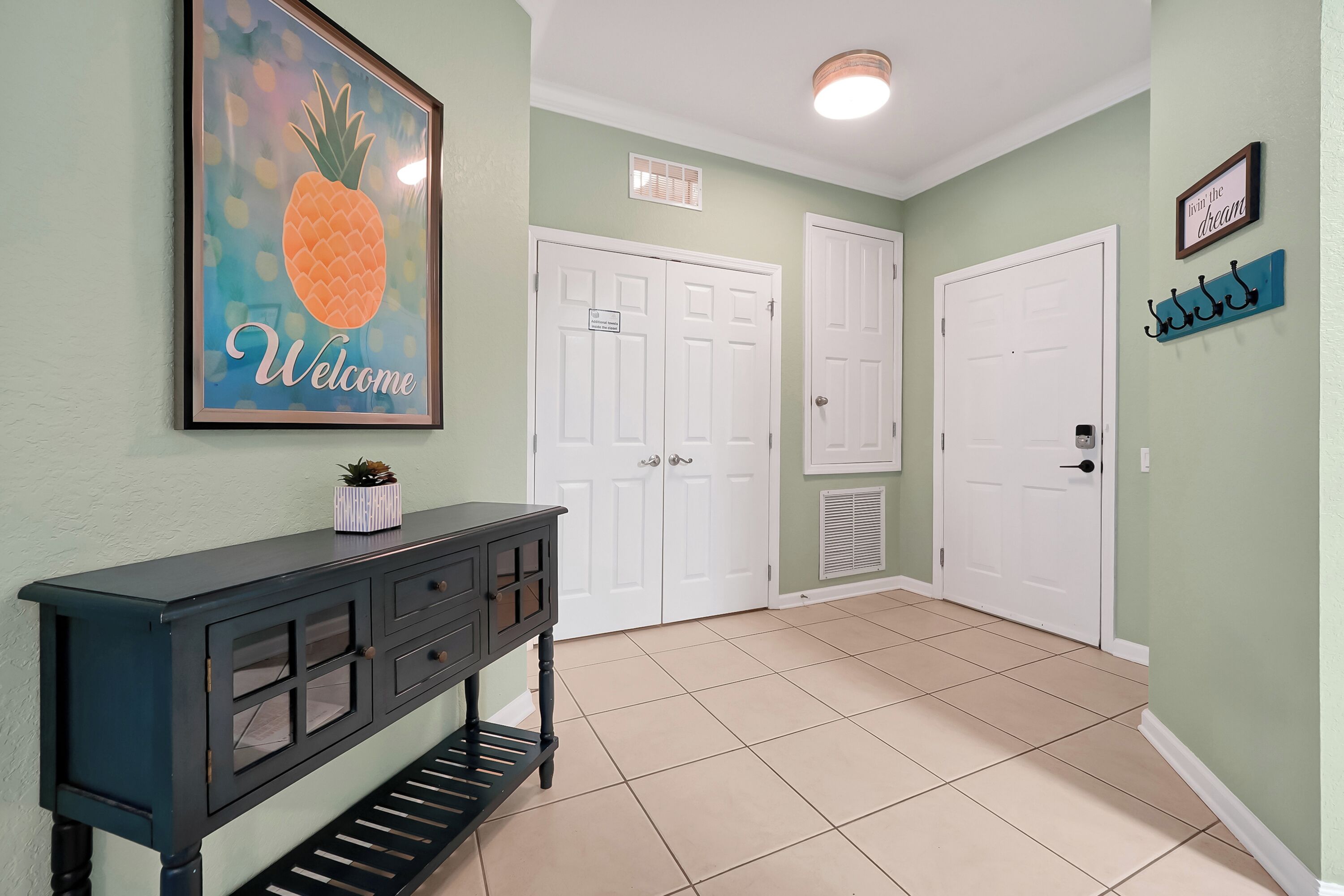 A hallway with a welcome sign, a dark console table, and white double doors.