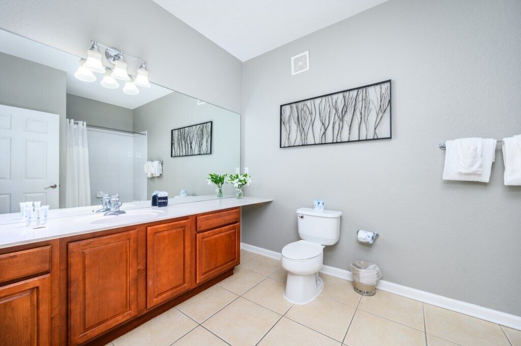 A modern bathroom with a large mirror, wooden cabinets, a white toilet, and a wall-mounted sink.