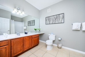 Een moderne badkamer met een grote spiegel, houten kastjes, een wit toilet en een wastafel op de muur bevestigd.
