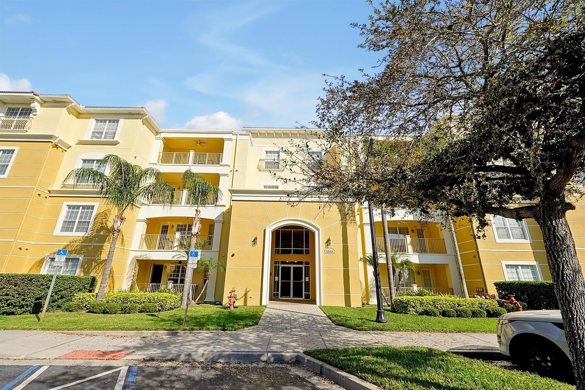 Un edificio amarillo de varios pisos con una entrada central, un hidrante y un letrero indicando acceso para sillas de ruedas.