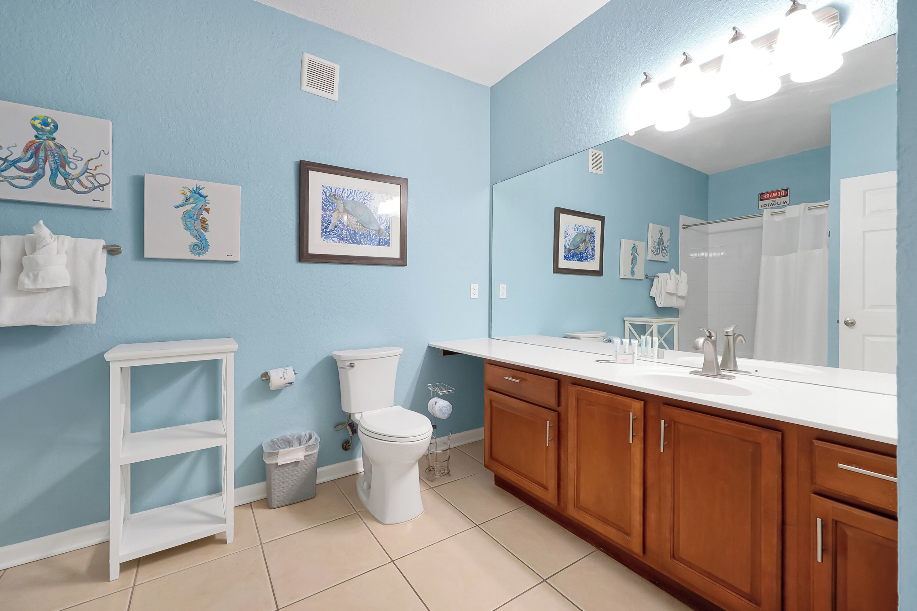 A bathroom with a toilet, sink, wooden cabinets, and framed artwork on the walls.