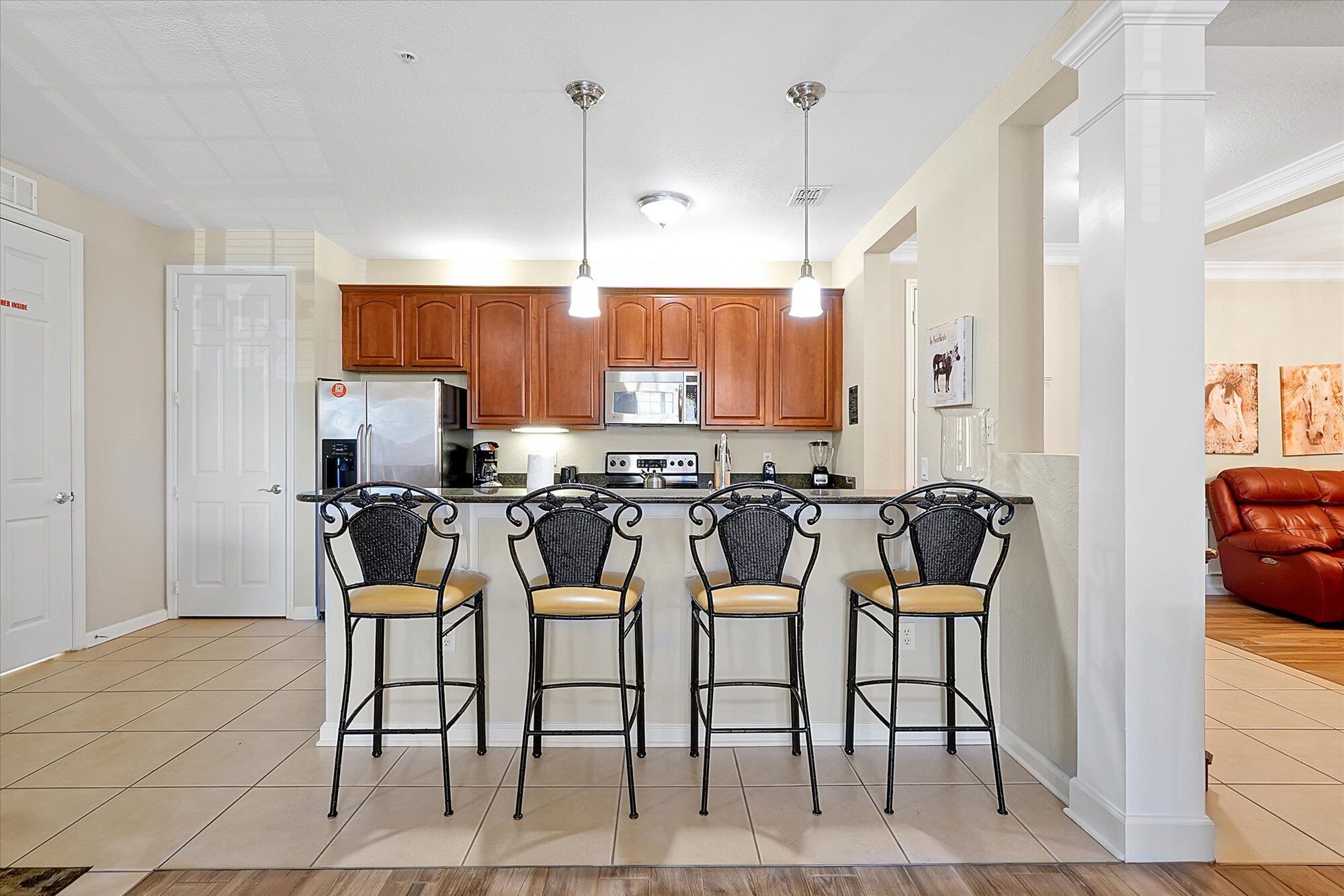 A kitchen with four bar stools, a refrigerator, a stove, and a microwave.
