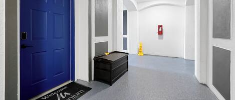 A hallway with a blue door labeled '110', a black bench, a yellow caution sign, and a fire extinguisher on the wall.