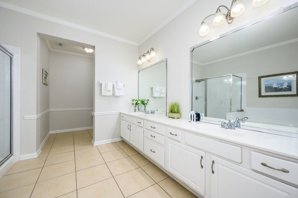 A bathroom with a large mirror, white cabinets, and a tiled floor.