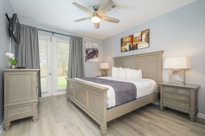 Een slaapkamer met een bed, nachtkastjes, een plafondventilator en een schilderij aan de muur.