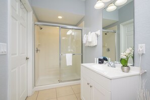 Een moderne badkamer met een glazen douchecabine, een wit wastafelmeubel met spiegel en een potorkidee.