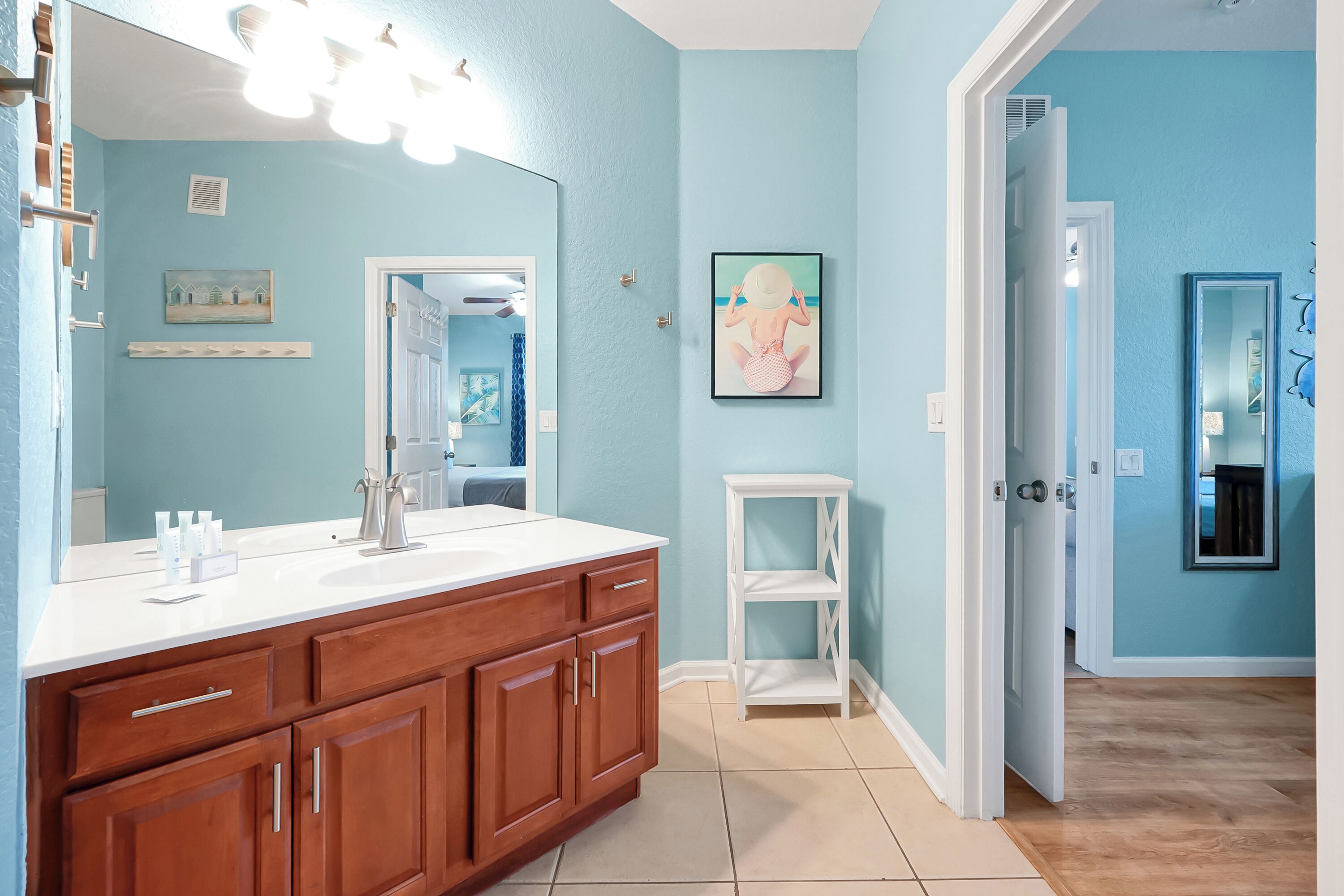A bathroom with a large mirror, wooden vanity, and a small white shelf.