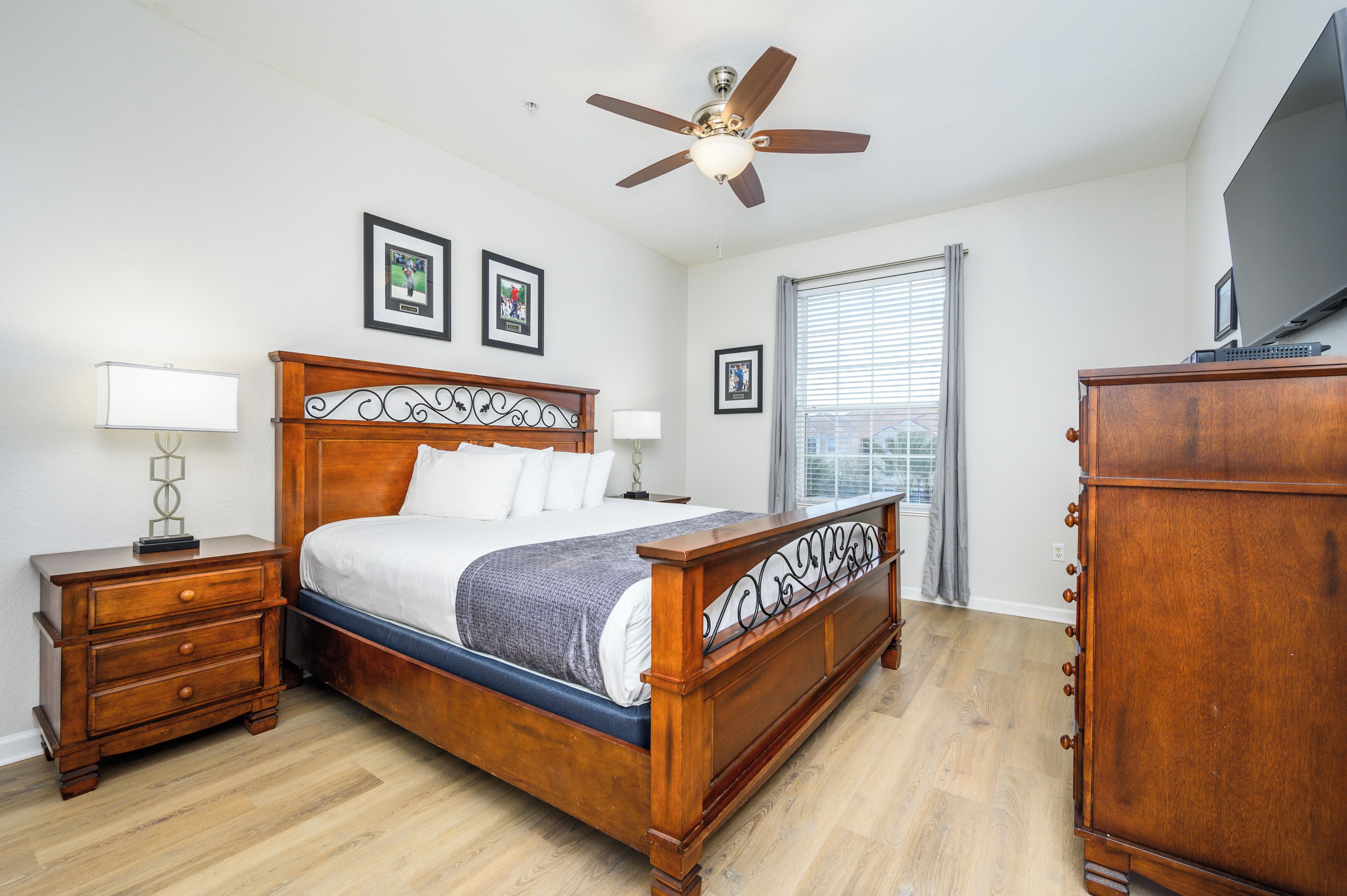 A bedroom with a wooden bed, nightstands, a dresser, a ceiling fan, and framed pictures on the wall.