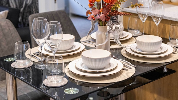Een eettafel gedekt met witte borden, kommen en wijnglazen, met een bloevas erbij.