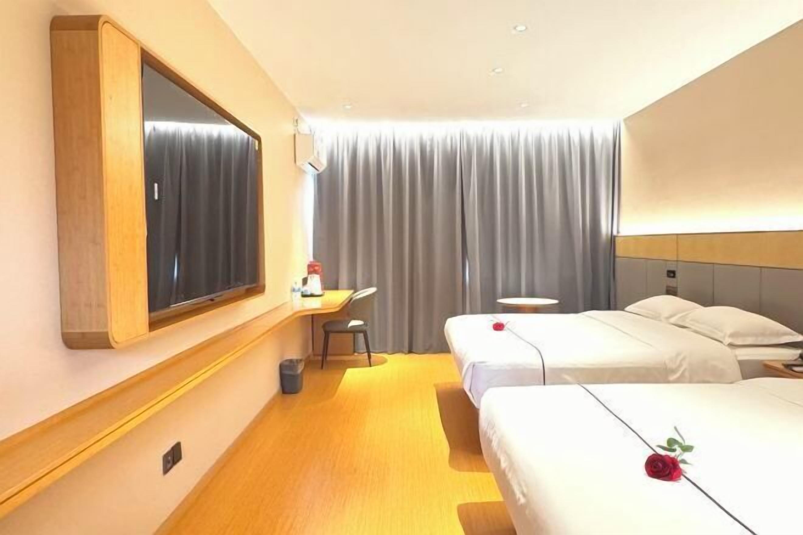 Habitación de hotel con dos camas, un escritorio, una silla, un espejo y un ventanal grande con cortinas.