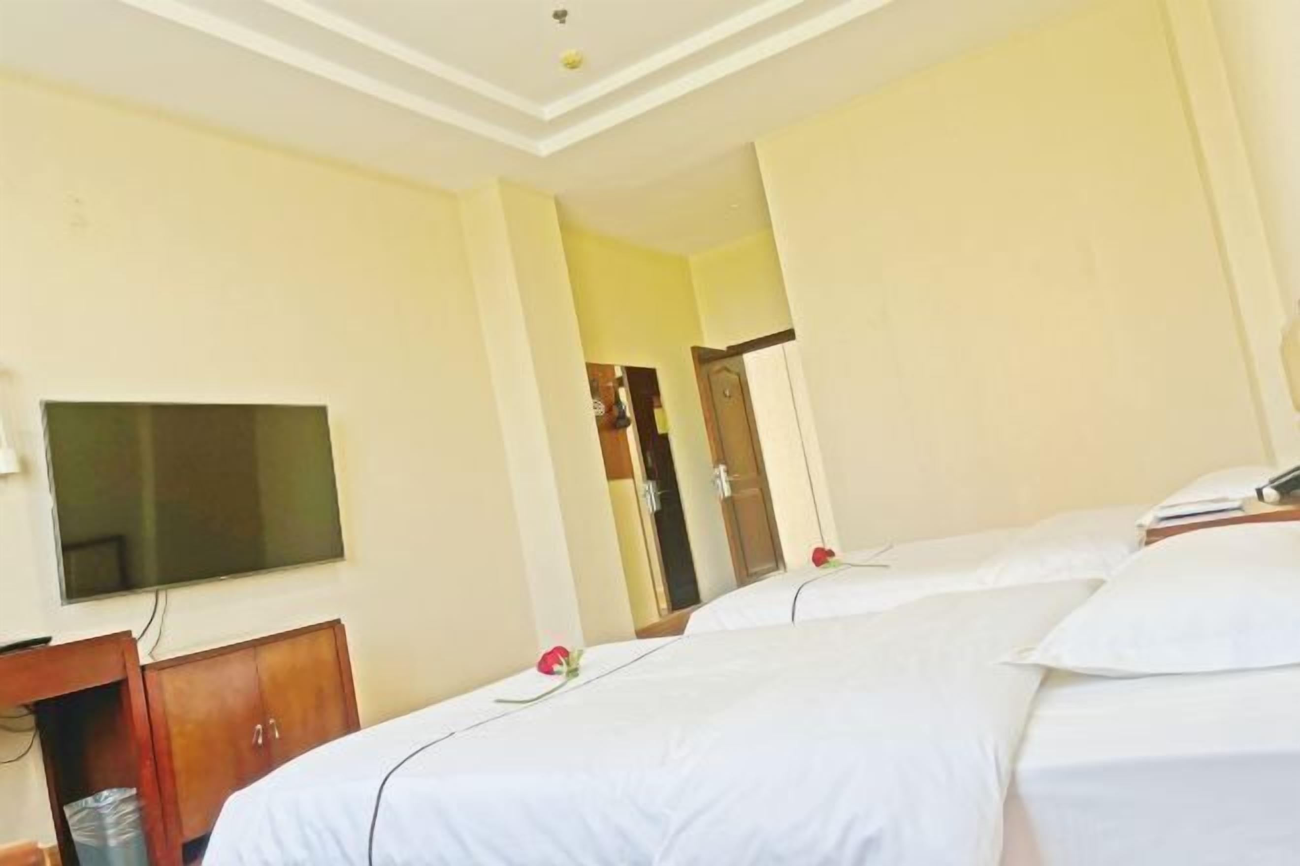 Habitación de hotel con dos camas, un televisor montado en la pared y un armario de madera.