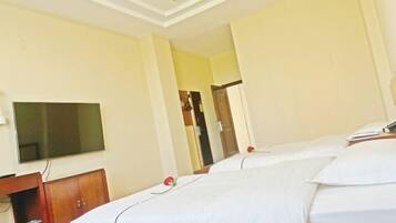 Habitación de hotel con dos camas, un televisor montado en la pared y un armario de madera.