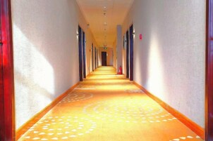 A hotel corridor with a patterned carpet, doors on both sides, and a fire extinguisher on the wall.