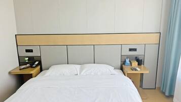Habitación de hotel con una cama grande, dos mesitas de noche, un cabecero y un buró con teléfono y control remoto.