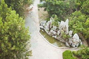 Un sendero conduce a un jardín rocoso con un estanque, rodeado de abundante vegetación.