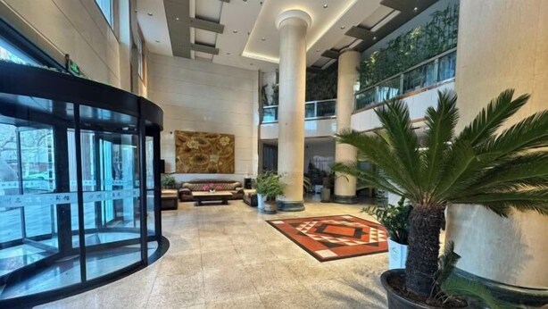 A spacious lobby with a central seating area, a glass elevator, and a large plant. - Mingya Hotel (Bohai International Plaza) (Binzhou)