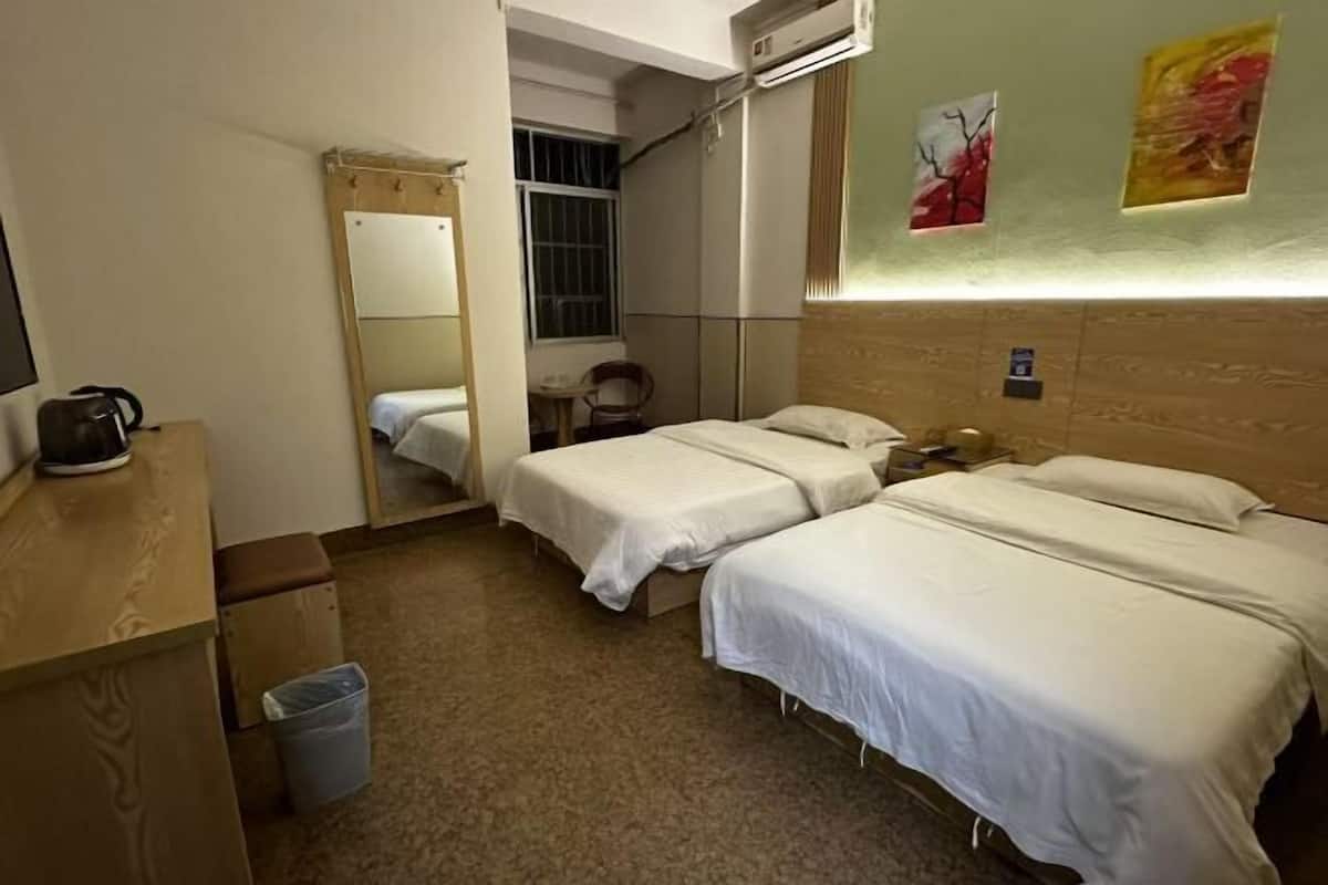 A hotel room with two single beds, a wooden desk, a chair, a trash bin, and a window with bars.