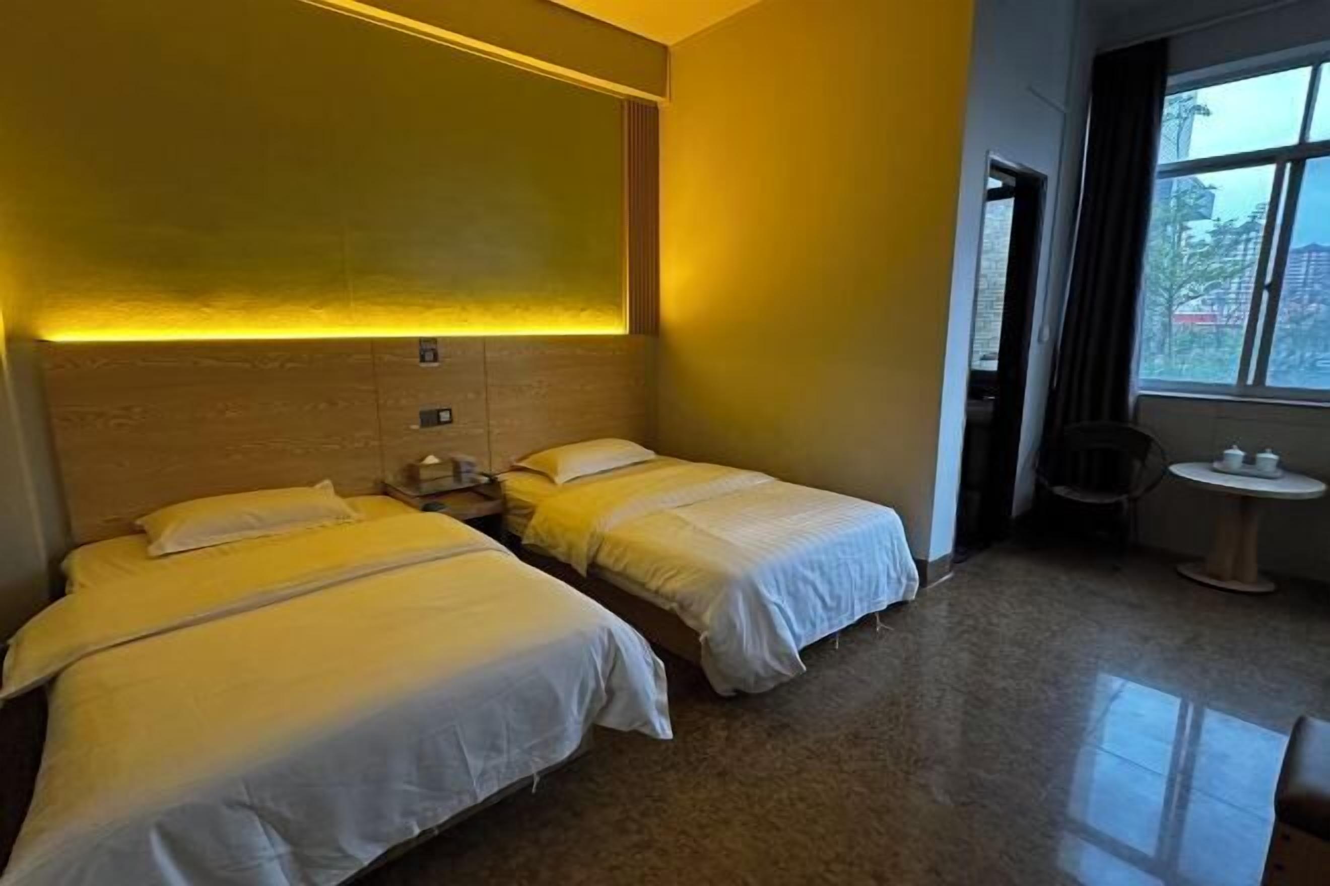 A hotel room with two beds, a small table, and a window with a view.