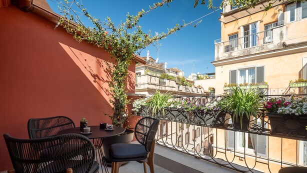 En balkon med fletstole, et lille bord og plantekasser.